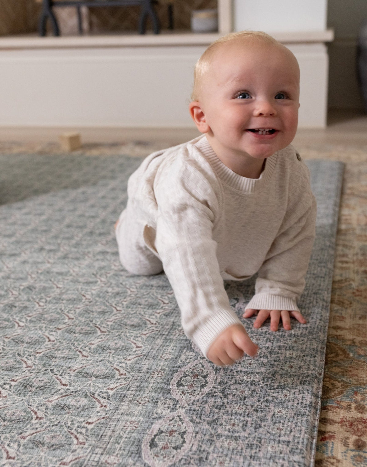 Baby crawling on a cushioned playmat with a Persian rug design