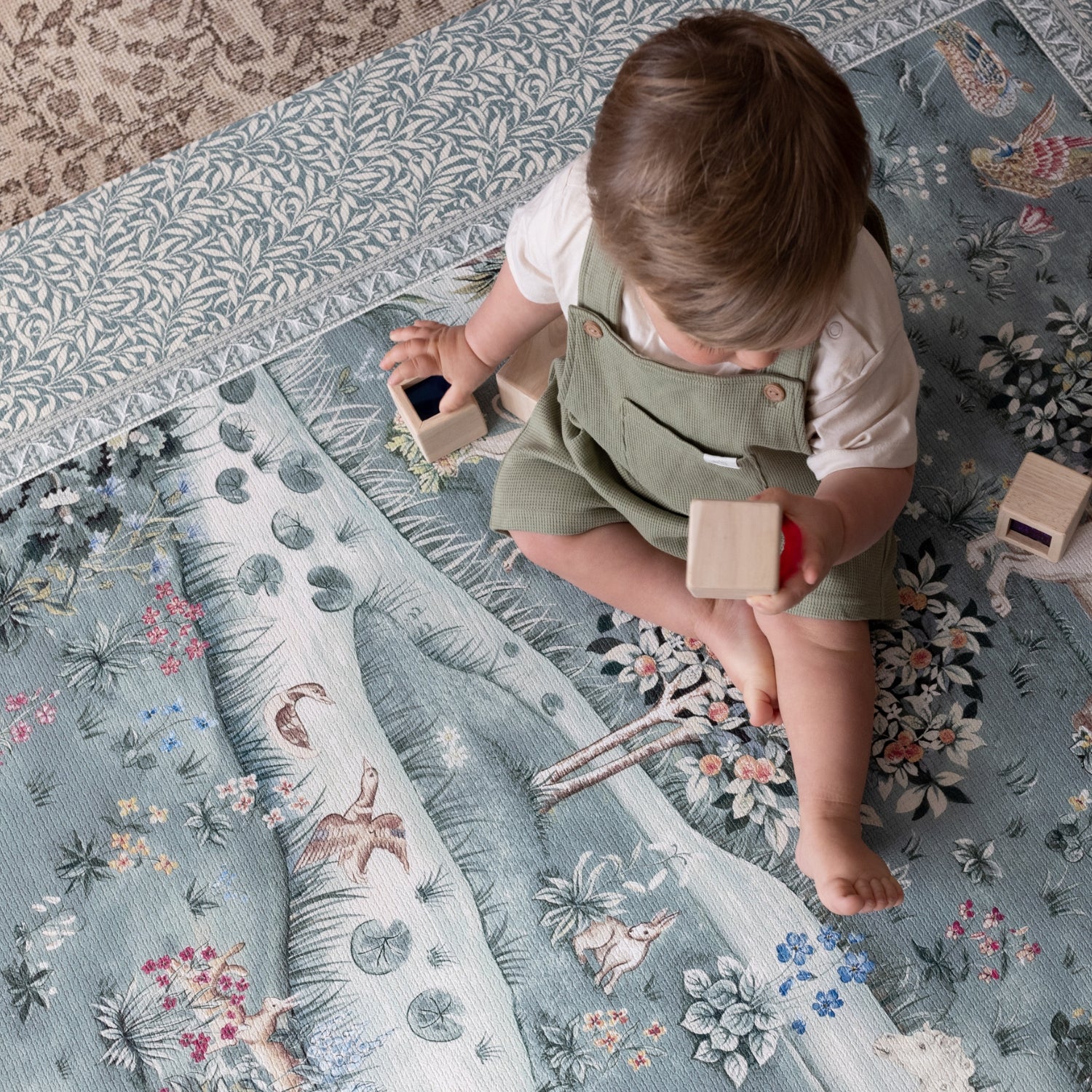 Toddler plays on a Totter + Tumble woodland animal play mat with botanical patterns; a one-piece, non-toxic foam playmat perfect for modern nurseries.