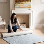 Rolling out a reversible blue and neutral baby playmat in a family room.