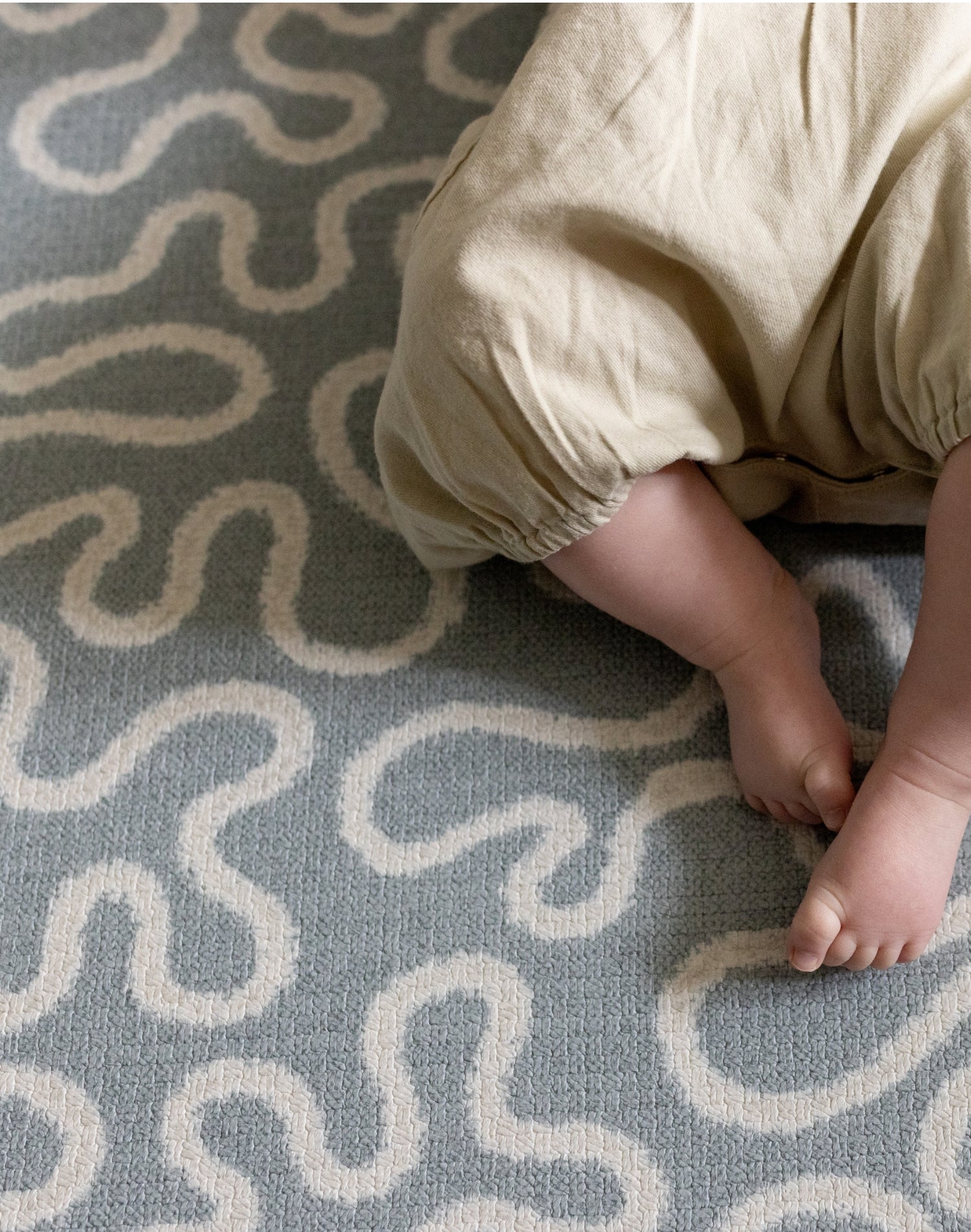 Baby's feet on a textured light blue rug with wavy patterns