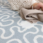 Person using a baby muslin to easily wipe clean a light blue and white patterned newborn playmat