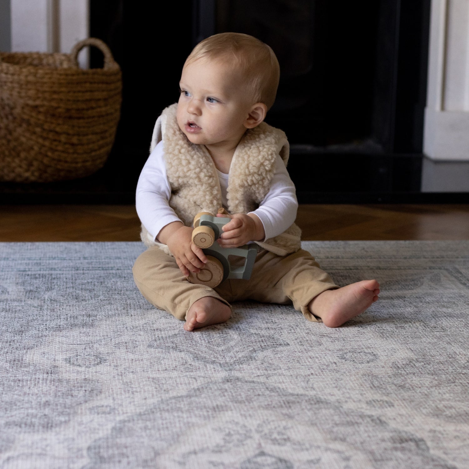 A baby sits up and is playing with a toy in the living room on a large playmat for infants
