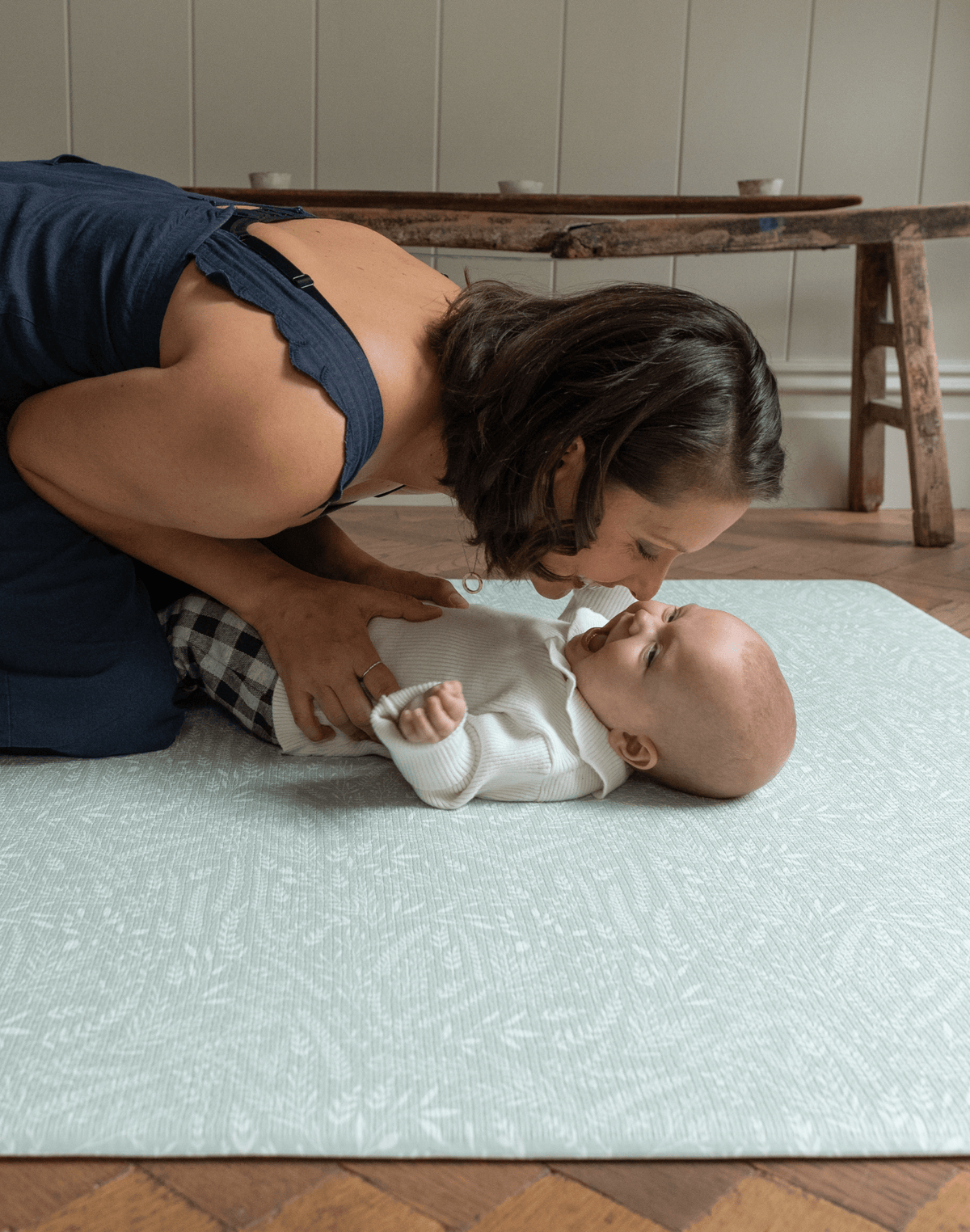 Mother kisses her little baby on the stylish green spielmatte by totter and tumble 