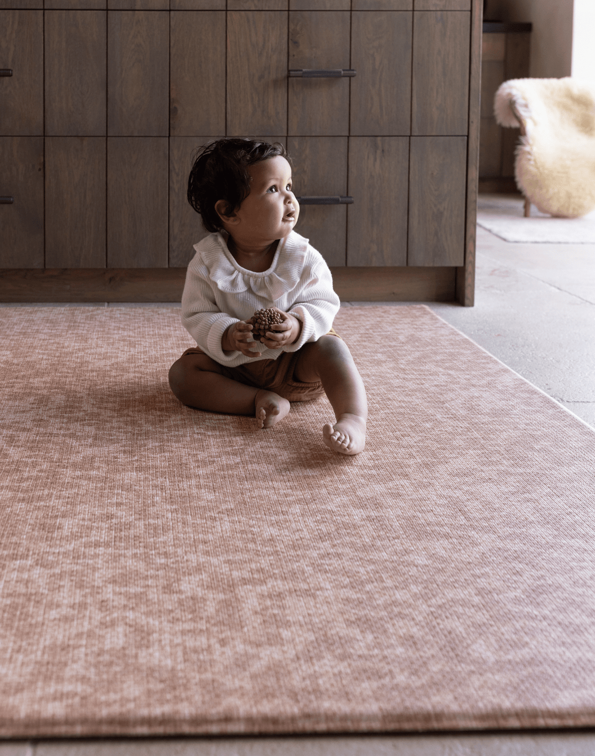 Baby sitting unaided on textured play mat thick memory foam design for support and protection on the floor soft orange play mat colour that blends seamlessly into modern family living spaces 