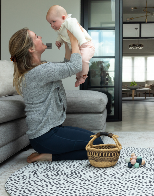 lady holds her baby while playing on the large round baby mat with a modern design 