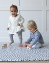 Toddlers play together on modern foam kids mat with a sensory motif