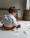 Little boy plays with wooden toy on beige baby play mat
