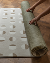Hands unroll the double sided play mat with olive kilim and tan solstice designs perfect for play areas at home 