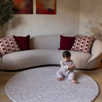 Baby girl sits comfortably on the extra large round padded playmat by totter and tumble with an animal print design to complement and add texture into stylish family homes
