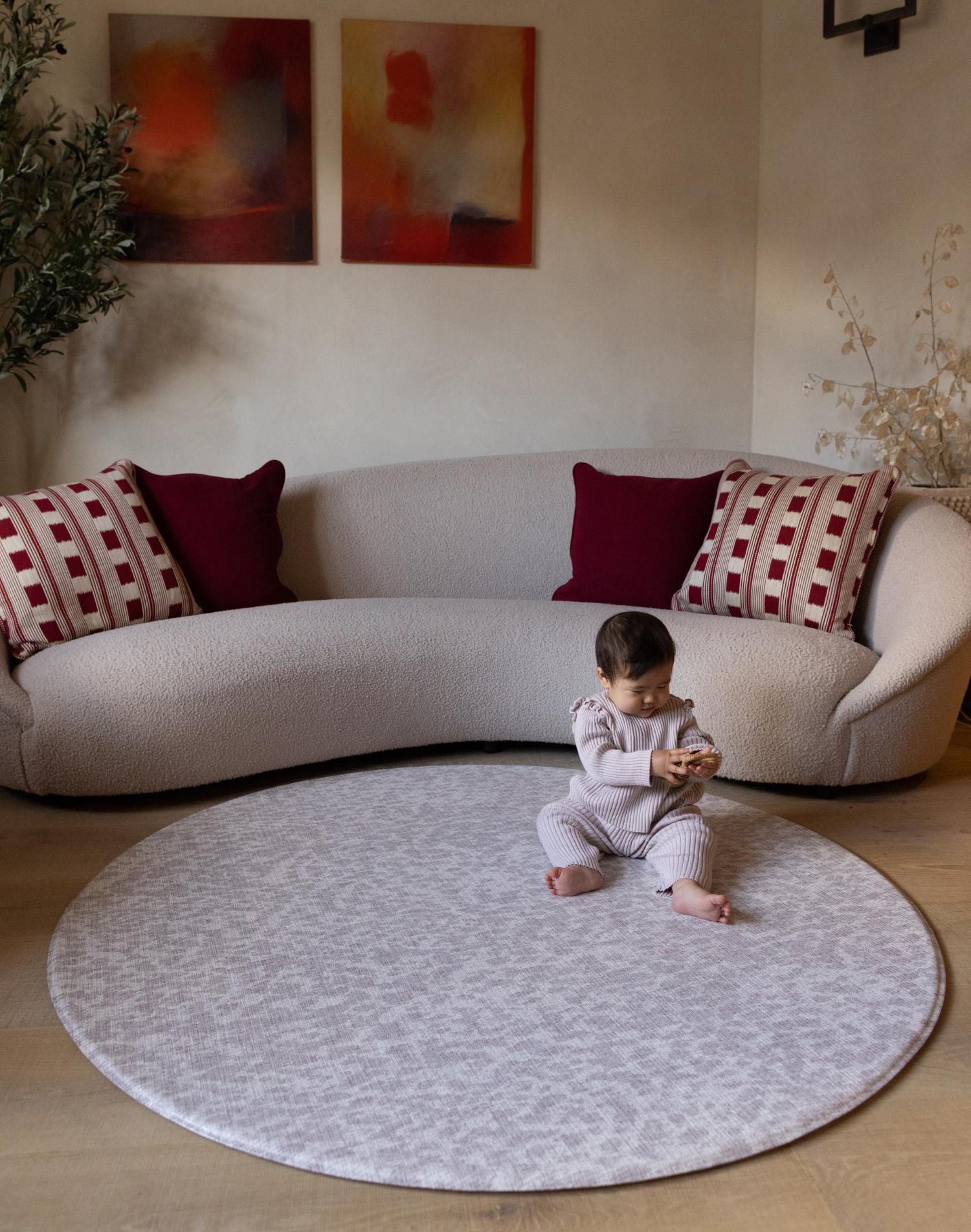 Baby girl sits comfortably on the extra large round padded playmat by totter and tumble with an animal print design to complement and add texture into stylish family homes