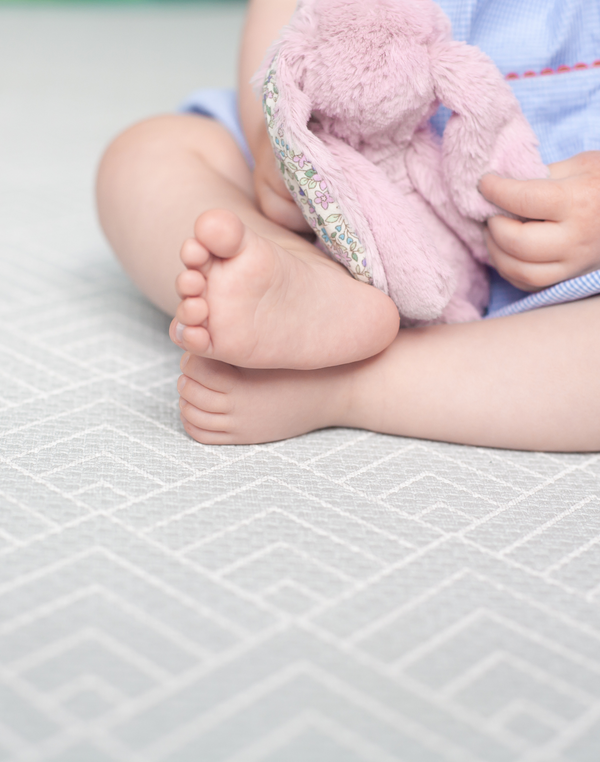 Baby sits safely on non toxic play mat designed from birth with a gentle grey design 