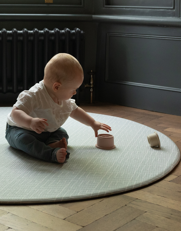 Baby plays with sustainable stacking cups on tapis de jeu rond