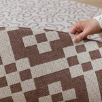 A hand folds over a Totter + Tumble reversible baby mat, revealing  a hexagon play mat design in brown on the reverse.