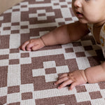 A baby crawls on a Totter + Tumble tummy time mat from the summer 2025 baby collection
