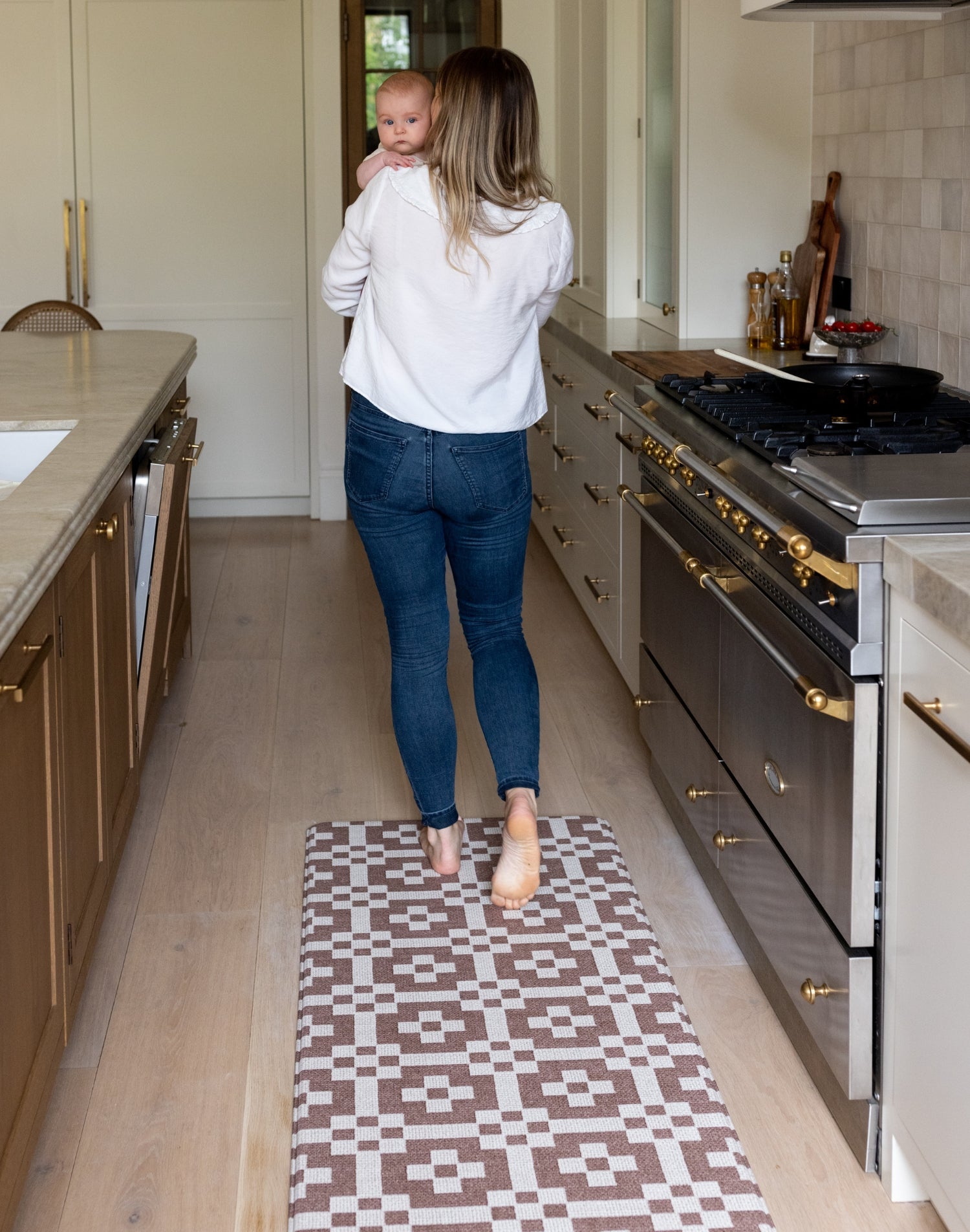 Woman holding a baby in a modern kitchen with a roasted umber playmat on the floor in a runner style