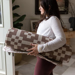 Woman holding a checkered yoga mat in a home setting