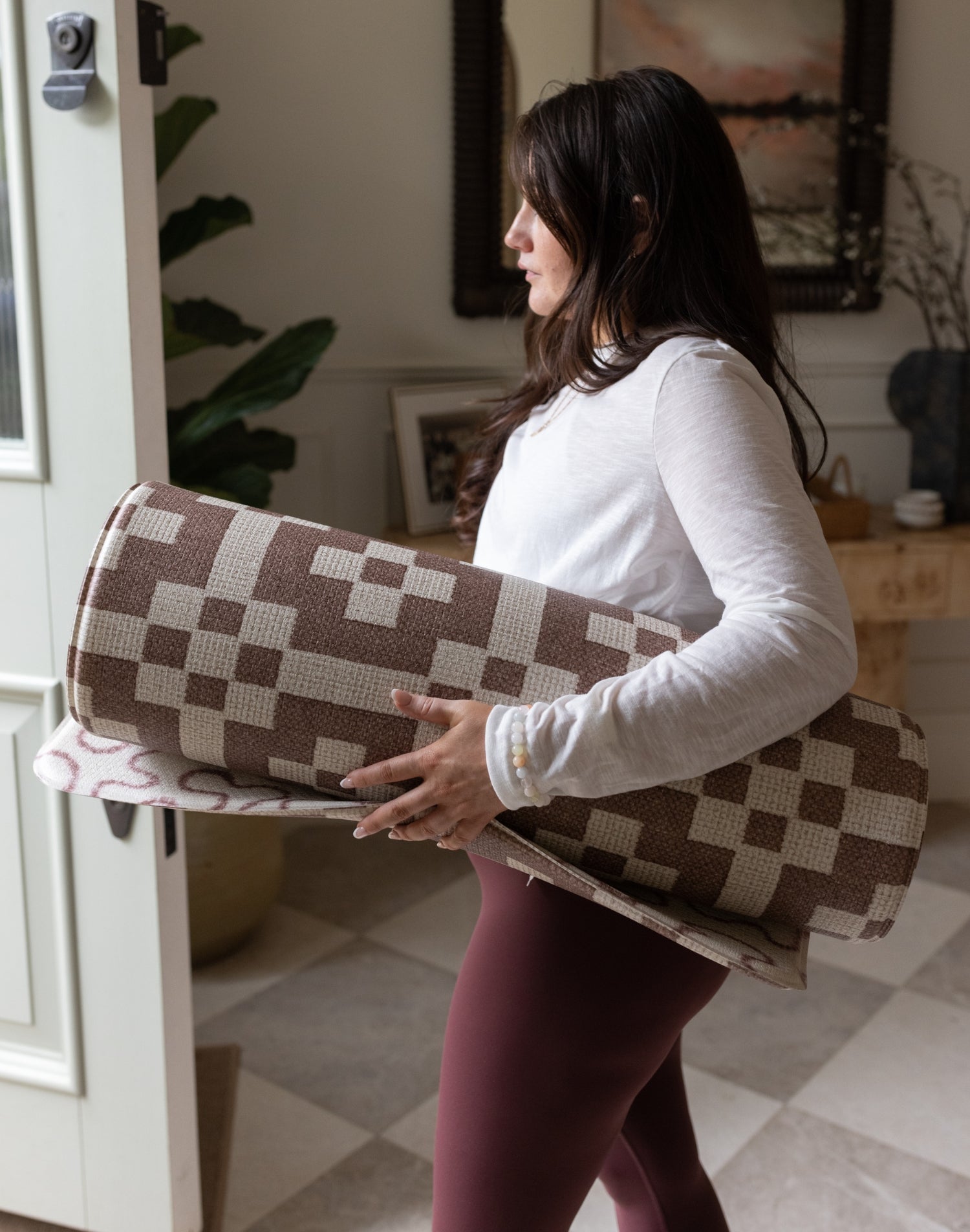 Woman holding a checkered yoga mat in a home setting