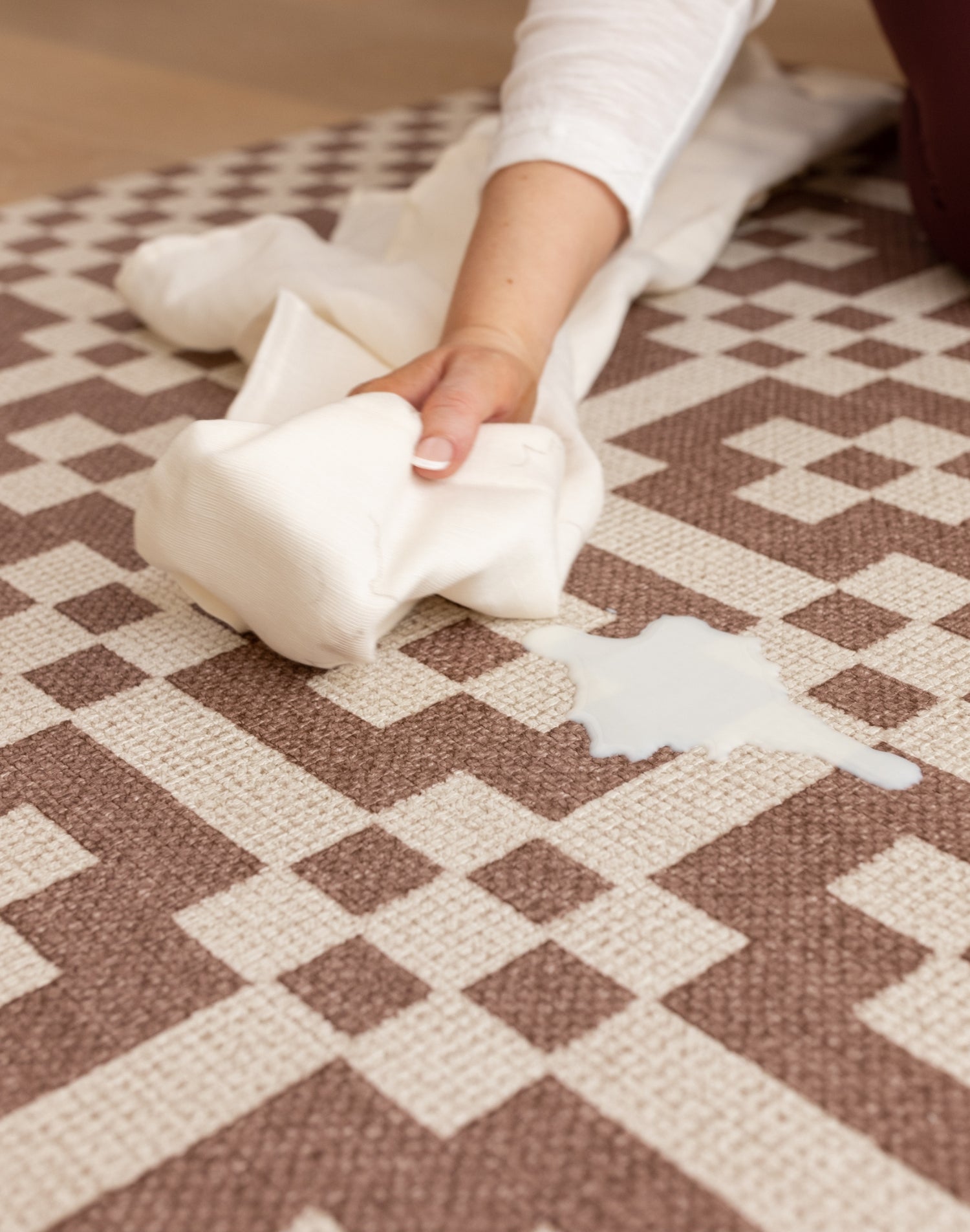Person cleaning a spill on a patterned play rug with a white cloth.