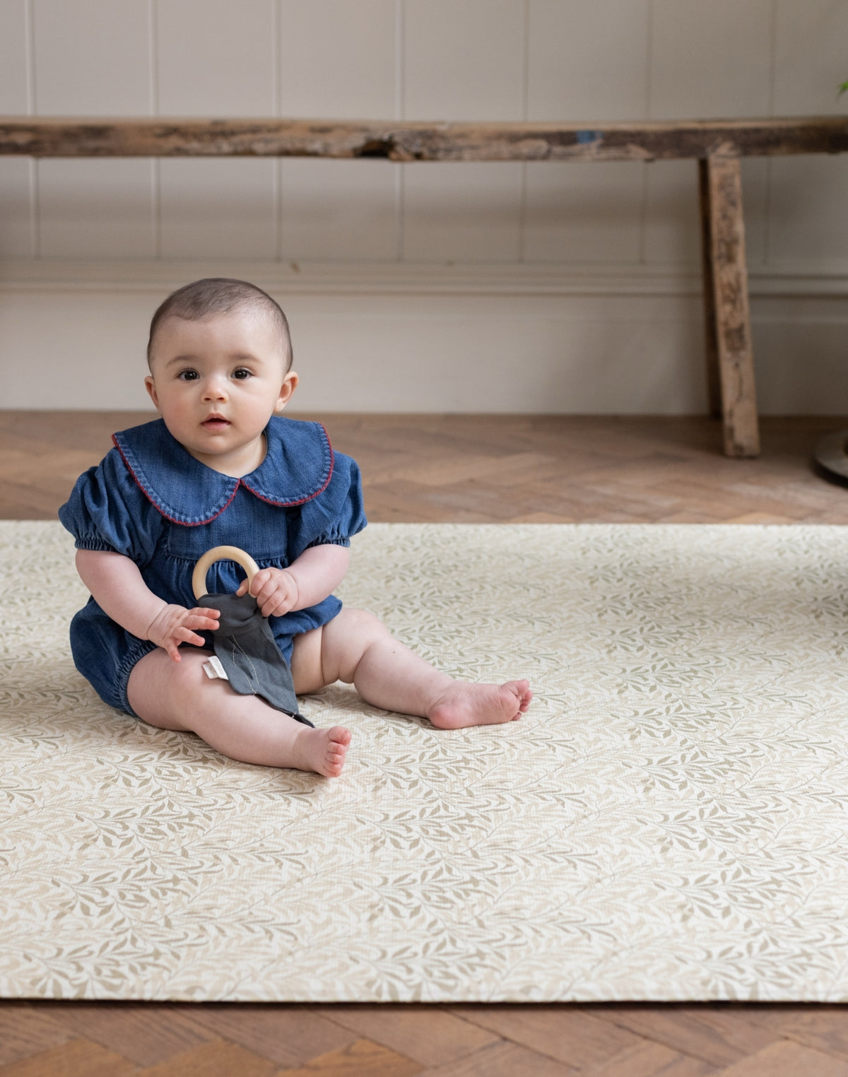 Baby sitting on a non toxic baby floor mat holding a toy in a room with hardwood floors.