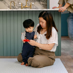 A family sat on the shell design, rug-like beachcomber playmat in a kitchen | SKU: 26 BEACH/GATHER XL, 26 BEACH/GATHER STD, 26 BEACH/GATHER COMP