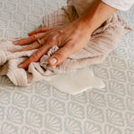 A close-up of a person's hand easily wiping up split milk on the beachcomber playmat | SKU: 26 BEACH/GATHER XL, 26 BEACH/GATHER STD, 26 BEACH/GATHER COMP