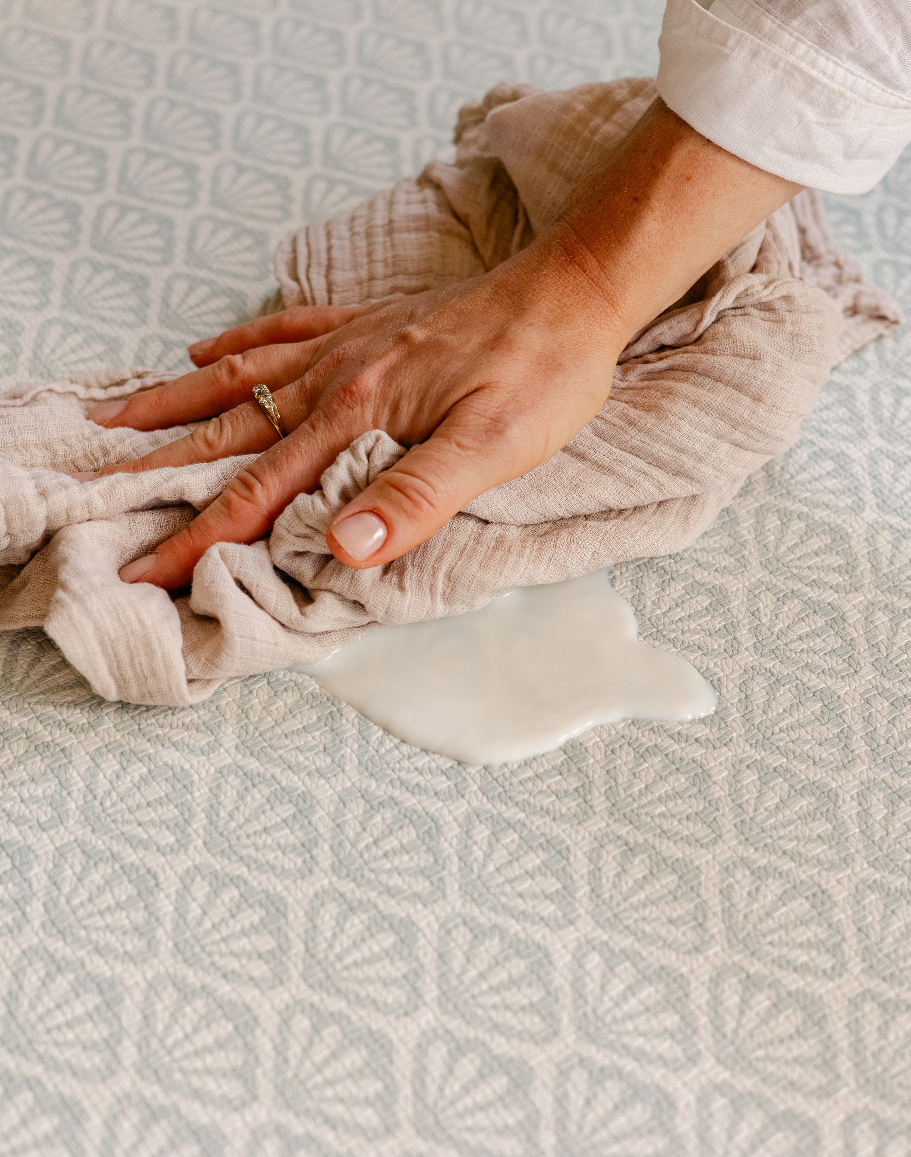 A close-up of a person's hand easily wiping up split milk on the beachcomber playmat | SKU: 26 BEACH/GATHER XL, 26 BEACH/GATHER STD, 26 BEACH/GATHER COMP