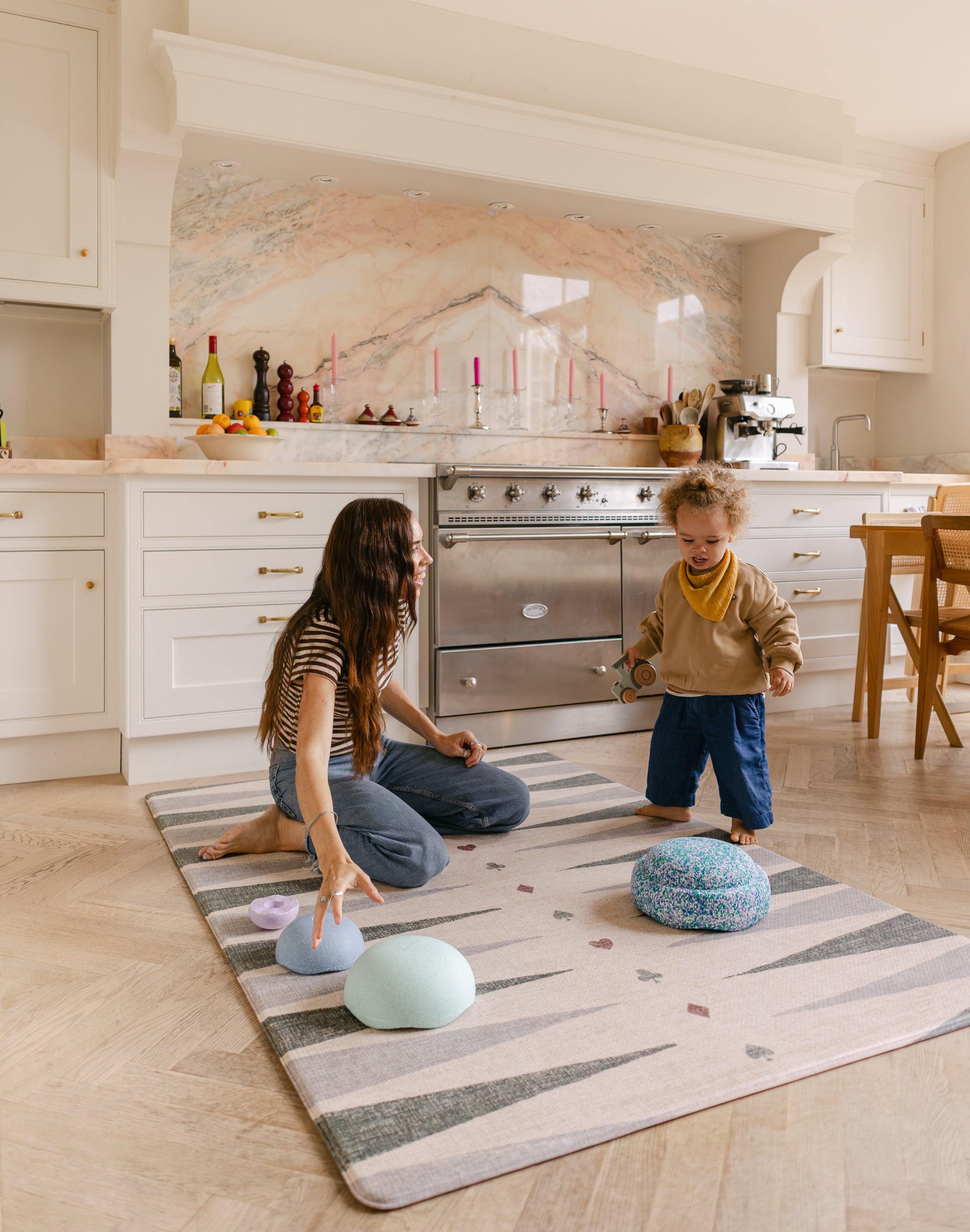 Mum and toddler on balance blocks on The Counter wipeable reversible memory foam playmat from Totter + Tumble in a bright kitchen