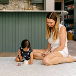 A woman sat playing comfortably and safely on a coastal inspired, British designed baby playmat from totter and tumble | SKU: 26 BEACH/GATHER XL, 26 BEACH/GATHER STD, 26 BEACH/GATHER COMP