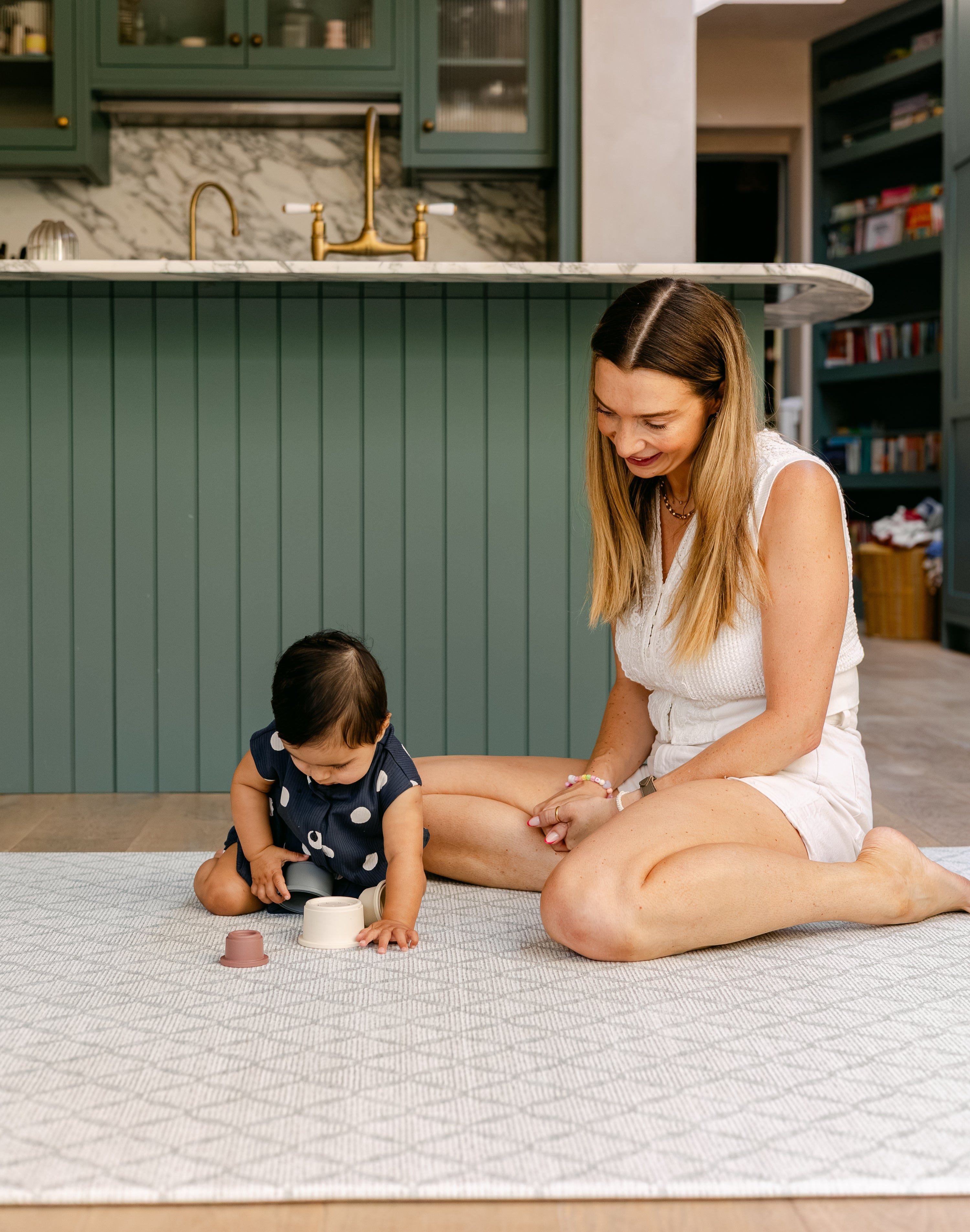 A woman sat playing comfortably and safely on a coastal inspired, British designed baby playmat from totter and tumble