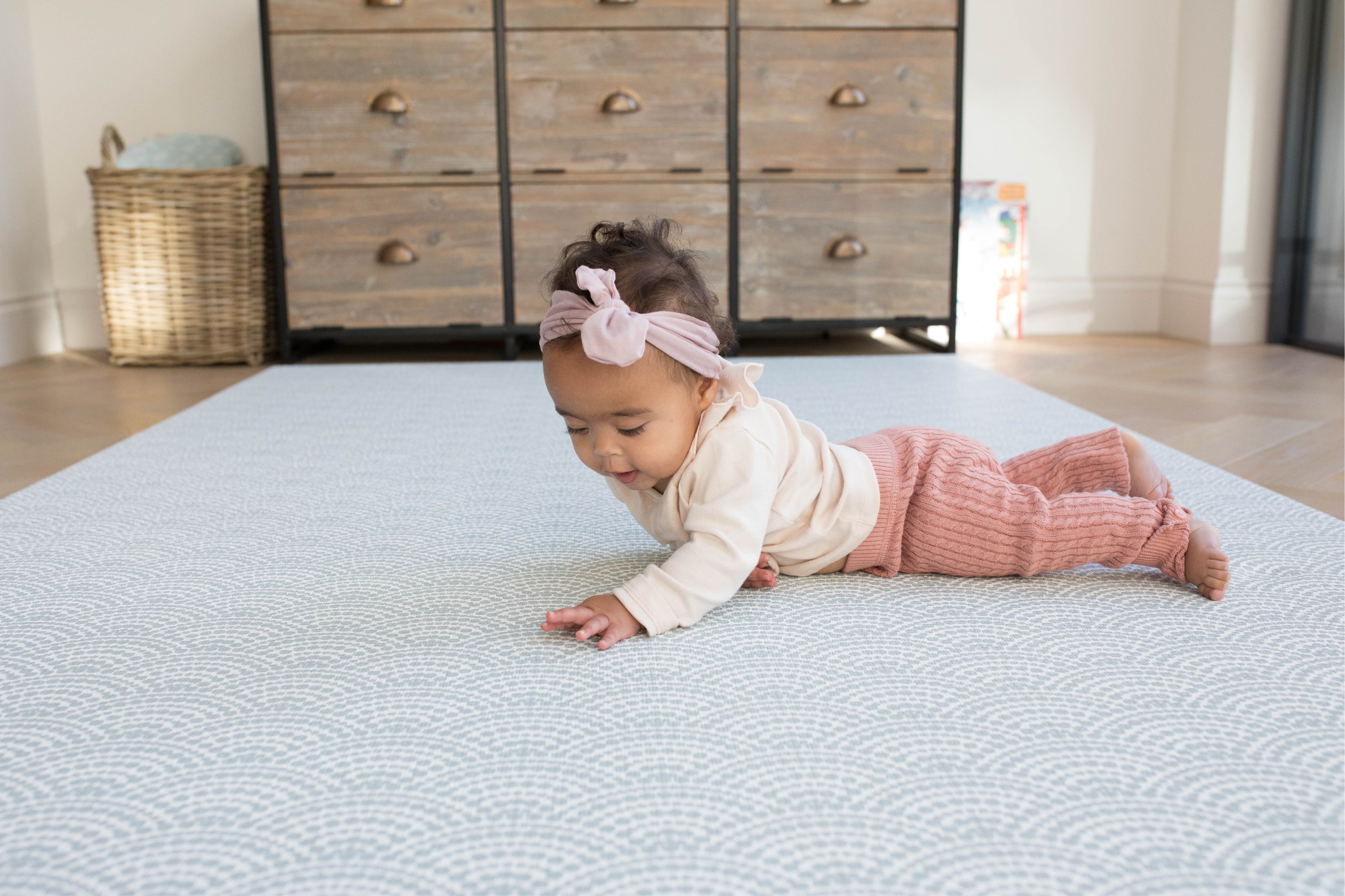 Baby lies on a soft, durable playmat in soft blue patterns