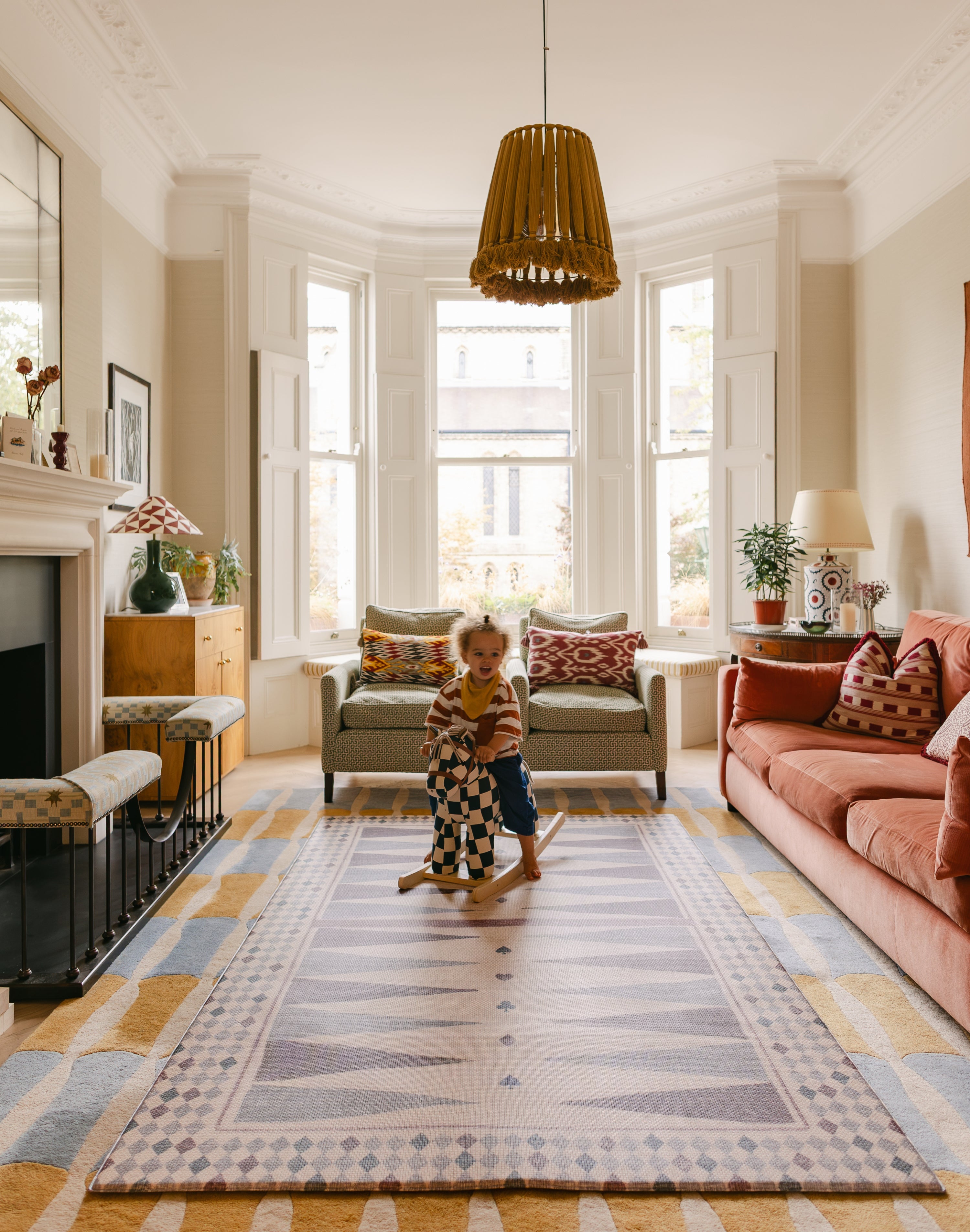 Child on rocking horse in bright living room on The Roller XL reversible memory foam playmat by Totter + Tumble, the largest one piece playmat on the market