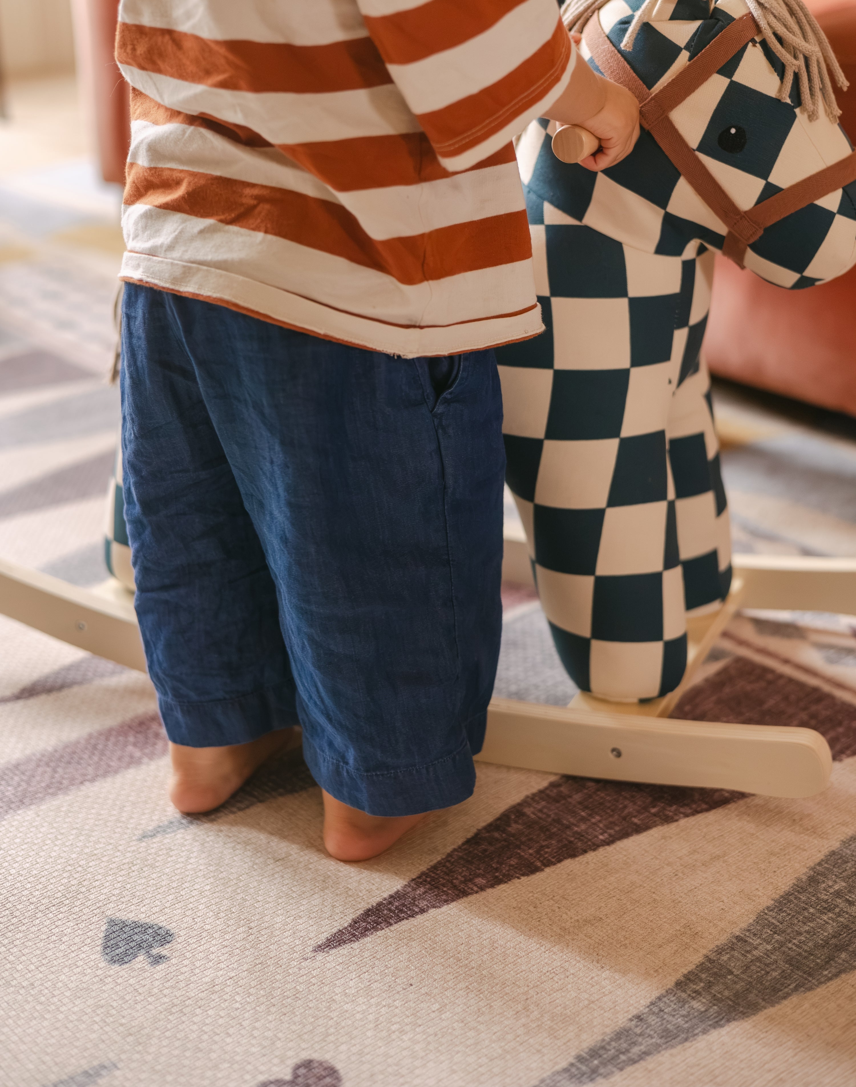 Child standing next to rocking horse on The Roller XL reversible memory foam playmat by Totter + Tumble, the largest one piece playmat on the market
