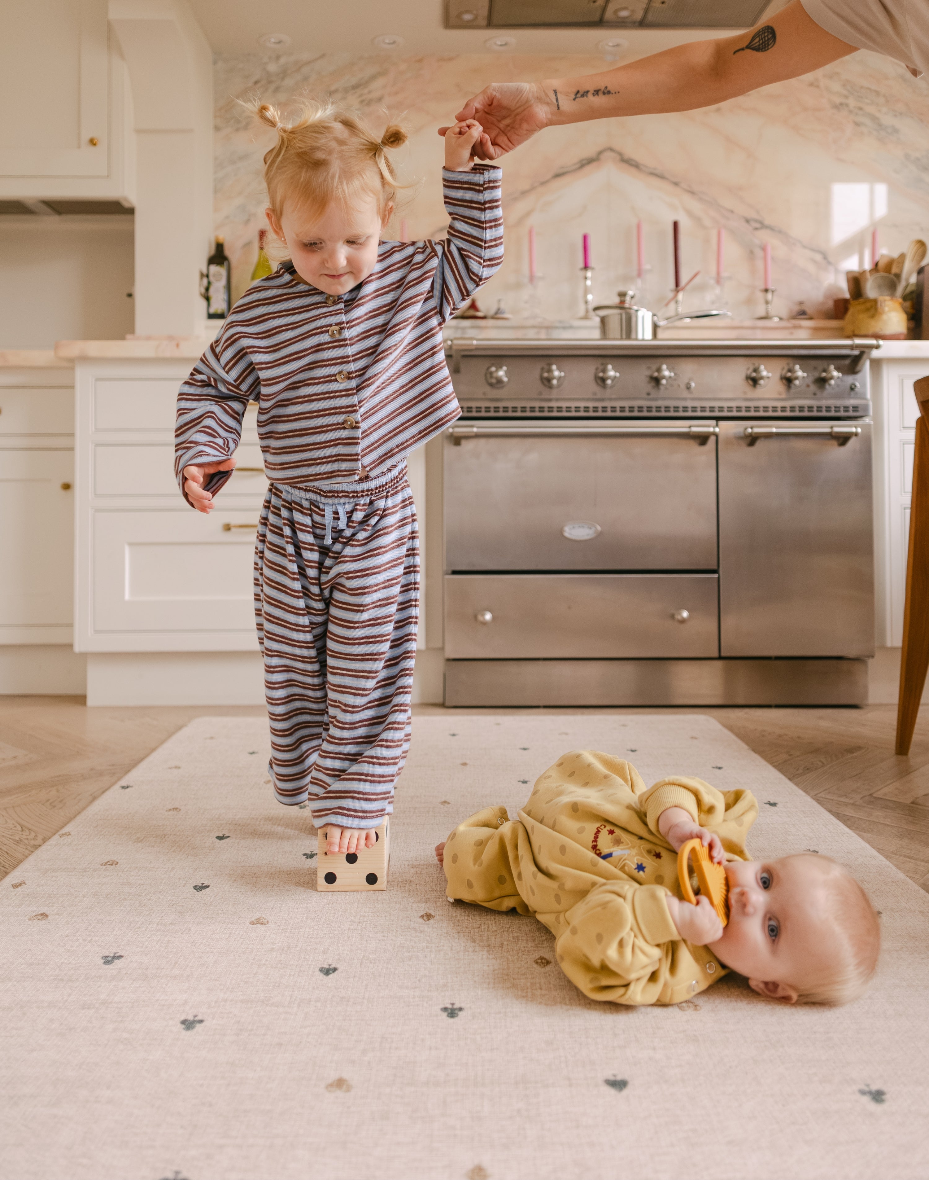 Toddler balancing on a dice on The Wildcard Totter + Tumble reversible memory foam playmat next to baby lying down
